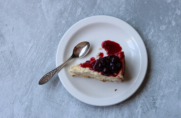Slice of cheesecake with berry sauce on white plate. Homemade cheesecake with blackcurrant jam on top. Sweet food close up photo. Space for text. 