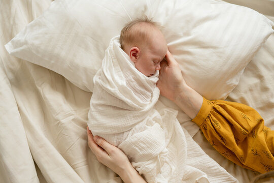 Unrecognizable woman comforting newborn baby on bed