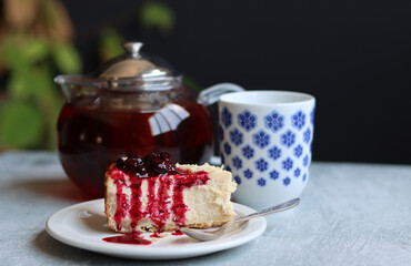 A piece of cherry cheesecake on a white plate and a teapot. Close up photo of homemade dessert. Sweet food concept. 