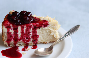 Slice of cheesecake with berry sauce on white plate. Homemade cheesecake with blackcurrant jam on top. Sweet food close up photo. Space for text. 