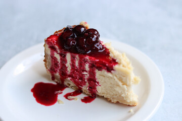 Slice of cheesecake with berry sauce on white plate. Homemade cheesecake with blackcurrant jam on top. Sweet food close up photo. Space for text. 
