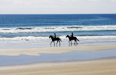 Fototapeta na wymiar People on the beach riding horses.