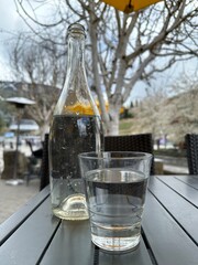 glass of water with a bottle of water sitting on a table at an outdoor cafe. 