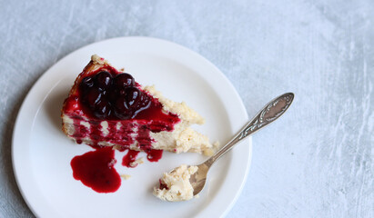 Slice of cheesecake with berry sauce on white plate. Homemade cheesecake with blackcurrant jam on top. Sweet food close up photo. Space for text. 