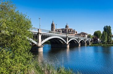 Fototapeta premium Perspective view of the bridge of Enrique Estevan over the Tormes river and the cathedral of Salamanca in the background with clear blue sky.