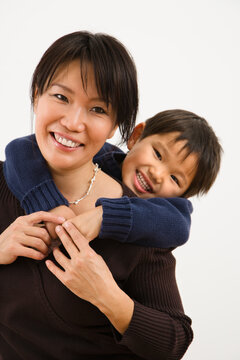 Asian mother with young son hugging her from behind smiling.