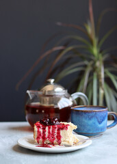 A piece of cherry cheesecake on a white plate and a teapot. Close up photo of homemade dessert. Sweet food concept. 