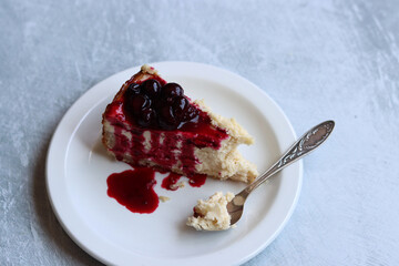 Slice of cheesecake with berry sauce on white plate. Homemade cheesecake with blackcurrant jam on top. Sweet food close up photo. Space for text. 