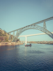 Fototapeta na wymiar Douro river with traditional sailing wine boat cruise, view of Maria Pia and Sao Joao bridges, typical architecture of cascade housing in sunhine. Rabelo boat in douro river, Porto, Portugal