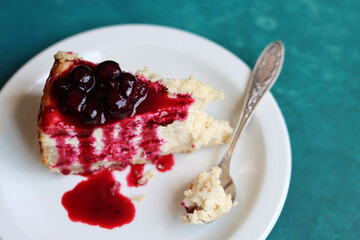 Slice of cheesecake with berry sauce on white plate. Homemade cheesecake with blackcurrant jam on top. Sweet food close up photo. Space for text. 