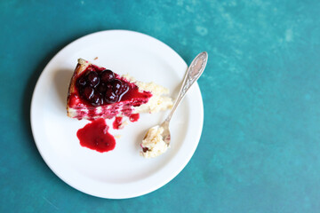 Slice of cheesecake with berry sauce on white plate. Homemade cheesecake with blackcurrant jam on top. Sweet food close up photo. Space for text. 