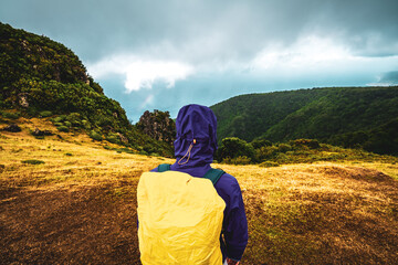 Back view of a backpacker woman in rainproof clothing watching the sea from a grassy mountain top. Fanal Forest, Madeira Island, Portugal, Europe.