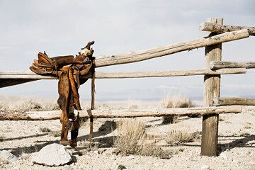 ranch scene - saddle on rural fence, vintage worn saddle in the dry and barren countryside