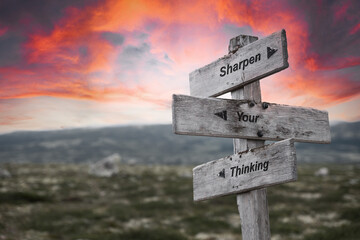 sharpen your thinking text quote on wooden signpost outdoors in nature. Pink dramatic skies in the background.