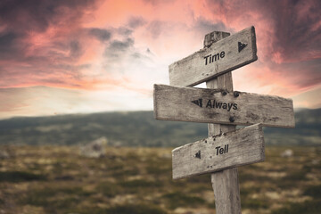 time always tell text quote on wooden signpost outdoors in nature. Pink dramatic skies in the background.