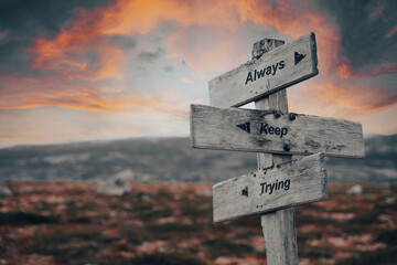 Always keep trying text quote on wooden signpost outdoors in nature. Pink dramatic skies in the background.