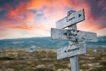 learn from mistakes text quote on wooden signpost outdoors in nature. Pink dramatic skies in the...
