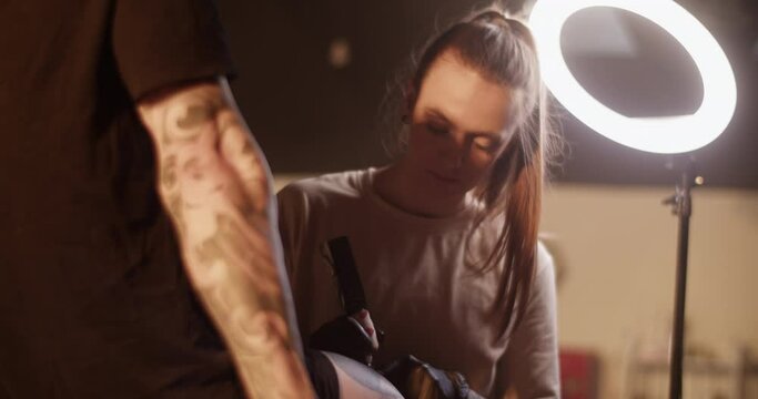 Female tattooist making tattoo on leg of male client with gun