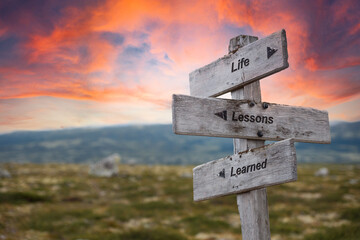 life lessons learned text quote on wooden signpost outdoors in nature. Pink dramatic skies in the background.
