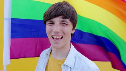 Young gay man smiling at camera over rainbow flag background. LGBT people concept