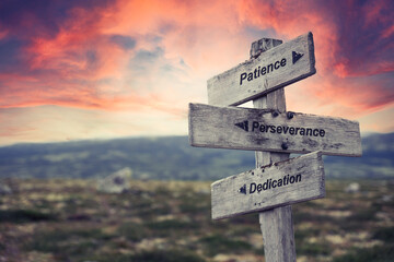 patience perseverance dedication text quote on wooden signpost outdoors in nature. Pink dramatic skies in the background.