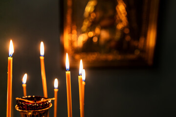 funeral candles burn on altar with blurred icon on background in dark church