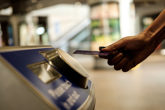 Female hand holding card over card reader machine in train station.