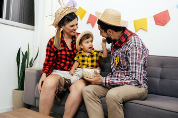 Brazilian Junina party at home. Family celebrating Festa Junina in the living room, wearing typical clothes and the wall decorated with colorful flags.