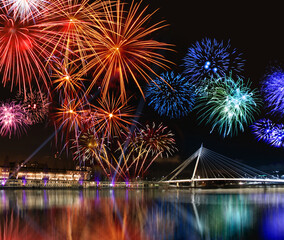 Fototapeta premium Colorful fireworks reflect from water, beautiful bridge scenery