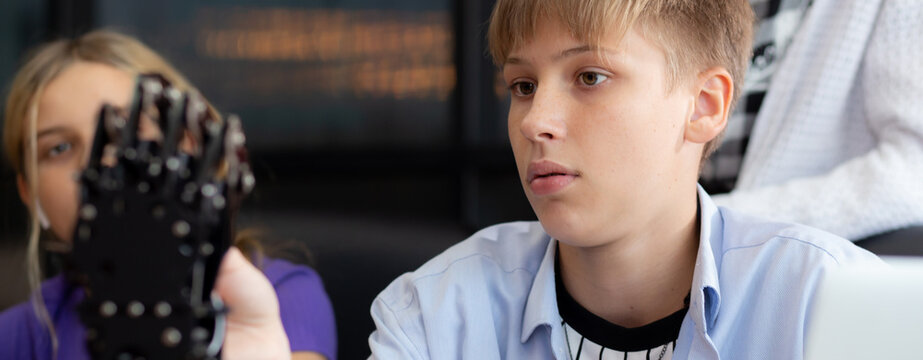 Caucasian two teenager students learning robotic arm in classroom together at school, boy and girl using controller study robot AI with cognition with teacher, education and development concept.