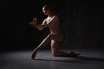 Ballerina in a beige bodysuit and pointe shoes. Dark background. Sculpted beautiful female body....