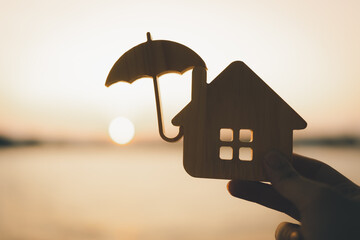 Wooden house model and real estate insurance ideas, individuals holding small umbrellas and sample...