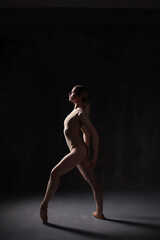 Ballerina in a beige bodysuit and pointe shoes. Dark background. Sculpted beautiful female body. Pose of a gymnast.