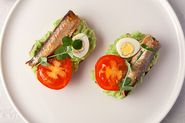 Sandwiches with sprats on toasted slices of bread. Sandwich with smoked sprat - fish, avocado and tomato. - obrazy, fototapety, plakaty
