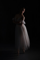 Professional ballerina dancing ballet.Ballerina in a white dress and pointe shoes. Dark background....
