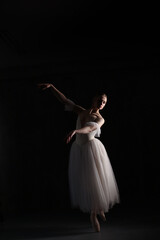 Professional ballerina dancing ballet.Ballerina in a white dress and pointe shoes. Dark background. Beautiful female body.