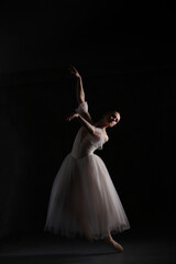 Fototapeta premium Professional ballerina dancing ballet.Ballerina in a white dress and pointe shoes. Dark background. Beautiful female body.