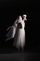 Fototapeta premium Professional ballerina dancing ballet.Ballerina in a white dress and pointe shoes. Dark background. Veil. Scene. Performance