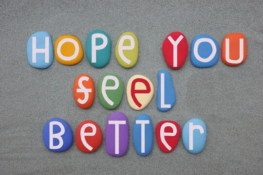 Hope you feel better, friendly message composed with multi colored stone letters over green sand