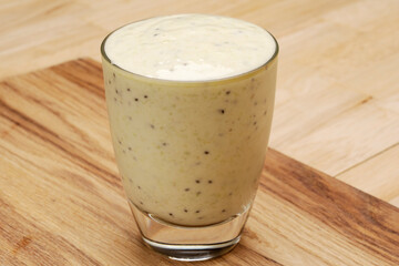 Light green kiwi and berry smoothie in a glass standing on a wooden table. 