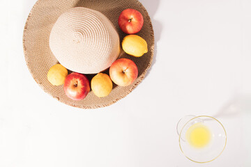 Summer tropical composition made of fresh organic fruit, a summer beach hat, and a cocktail glass full of juice against a white background. Minimal nature flat lay.