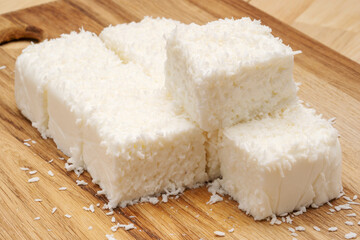 White tender milk dessert with coconut flakes on a wooden cutting board. 