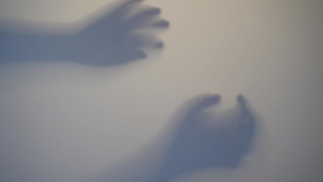 Shadow Blur of a horror man behind frosted glass. Blurred hand, body shape abstraction and one palm. Reflection of the silhouette through the light.
