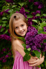 a beautiful happy smiling blonde girl with long hair in a pink dress with a purple bouquet of lilacs in her hands stands against the background of a lilac bush