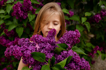 a large portrait of a blonde girl with a large bouquet of purple lilac who enjoys the fragrance of flowers