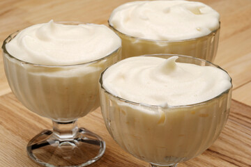 Airy white mousse in dishes standing on a wooden table. 