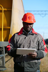 African american railway man with tablet computer at freight train terminal