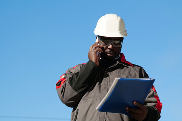 African american worker looks in work papers and talks on smartphone