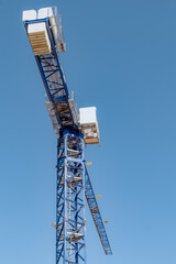High-rise construction crane with a long blue boom against the blue clear sky. Vertical
