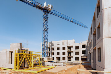Fototapeta na wymiar High-rise building crane with a long arrow of blue color on blue clear sky above a concrete building under construction with solid walls